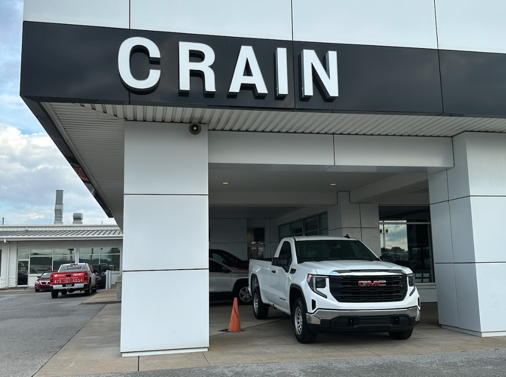 White GMC pickup truck parked under the Crain dealership sign in Springdale